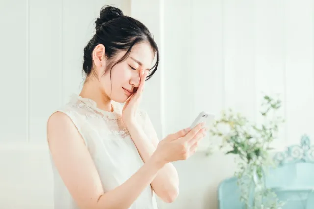 スマートフォンを見て首こりを感じている新宿のデスクワーク女性